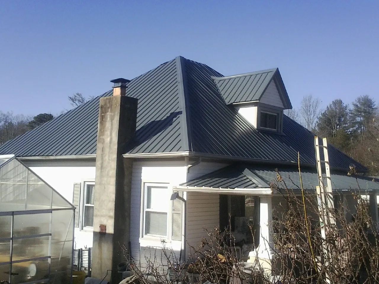 Dark blue standing seam metal roof on a white farmhouse with dormer — Slate & Tile Roof Repair by Roofing Brothers in Winnsboro