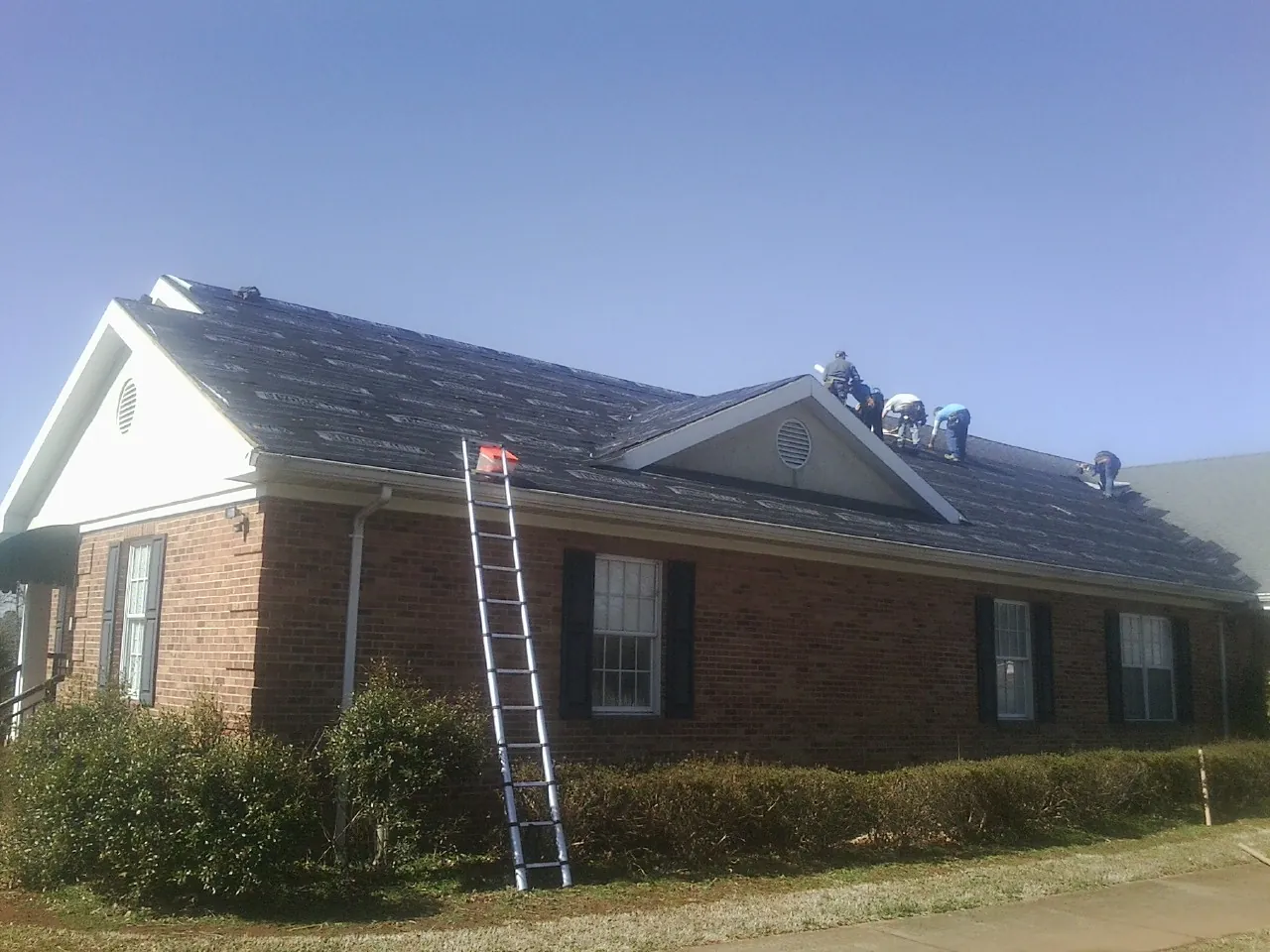Crew tearing shingles off a brick ranch roof with a ladder set — Metal Roof Repair work by our crew in Winnsboro