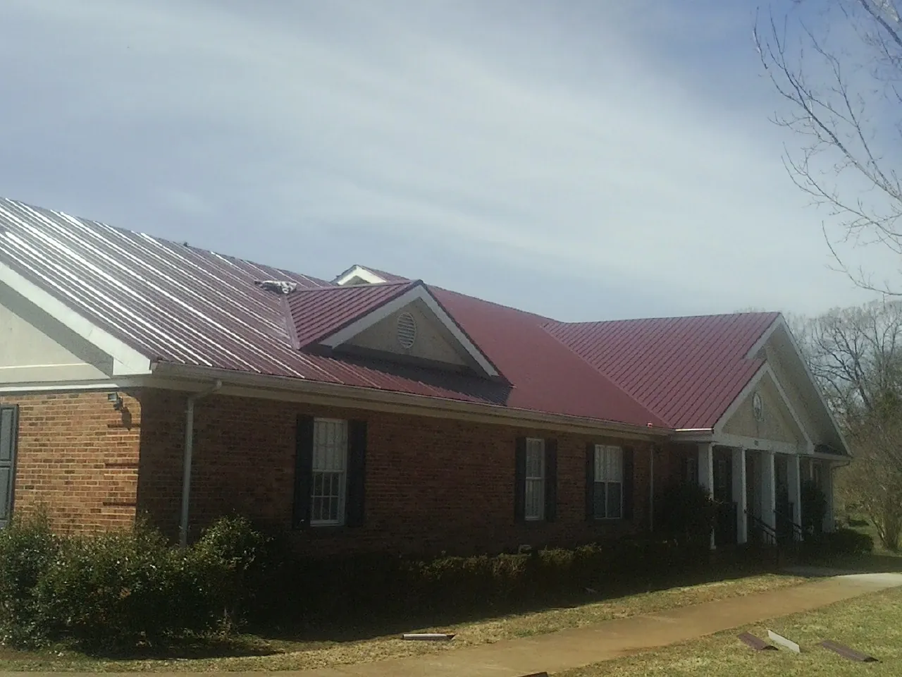 Red metal roof with gabled entries on a long brick building, from a Hail Damage Roof Repair job in Winnsboro