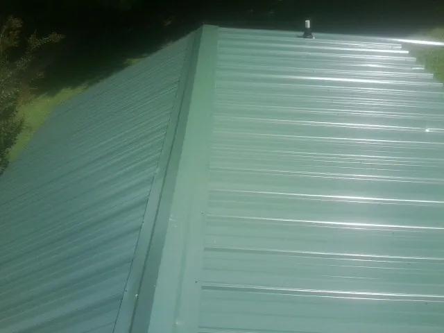 New green metal panels meeting at the ridge of a roof — Flat Roof Repair work by our crew in Winnsboro