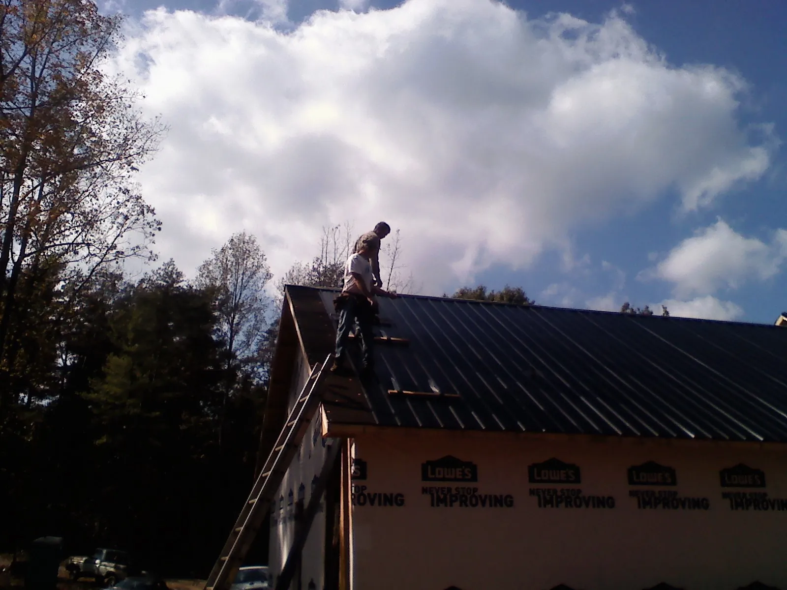 Roofer fastening dark metal panels high against a cloudy sky, from a Roof Inspection job in Winnsboro
