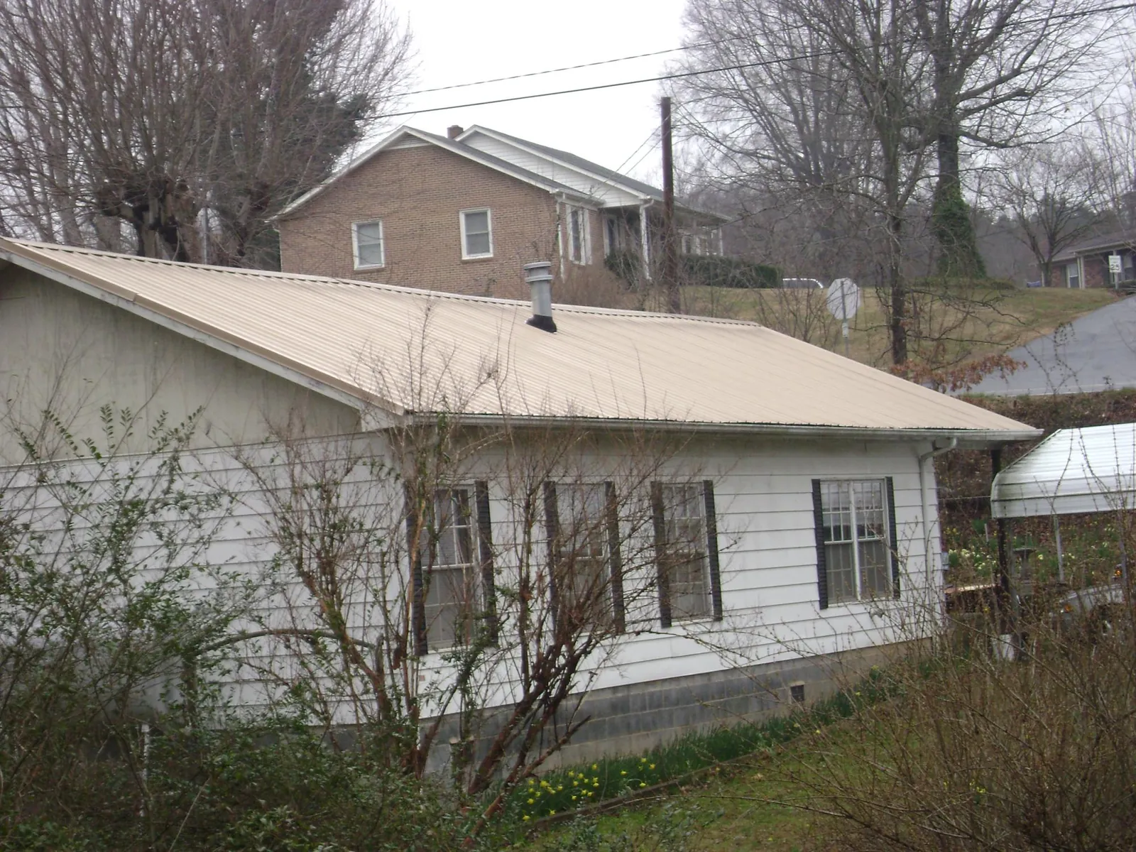 Tan metal roof on a white sided house set into a hillside — Commercial Roofing by Roofing Brothers in Winnsboro